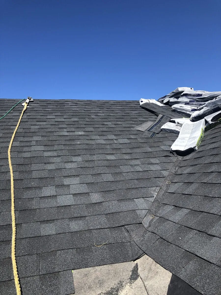 Steep asphalt roof slope worked with a safety rope, new bundles staged at the ridge